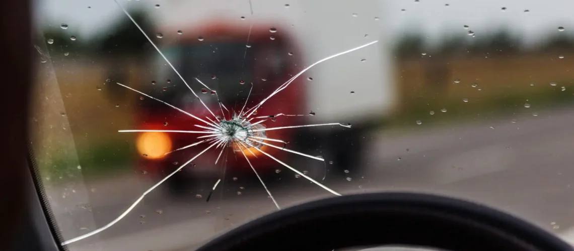 Broken windshield of a car. A web of radial splits, cracks on the triplex windshield. Broken car windshield, damaged glass with traces of oncoming stone on road or from bullet trace in car glass