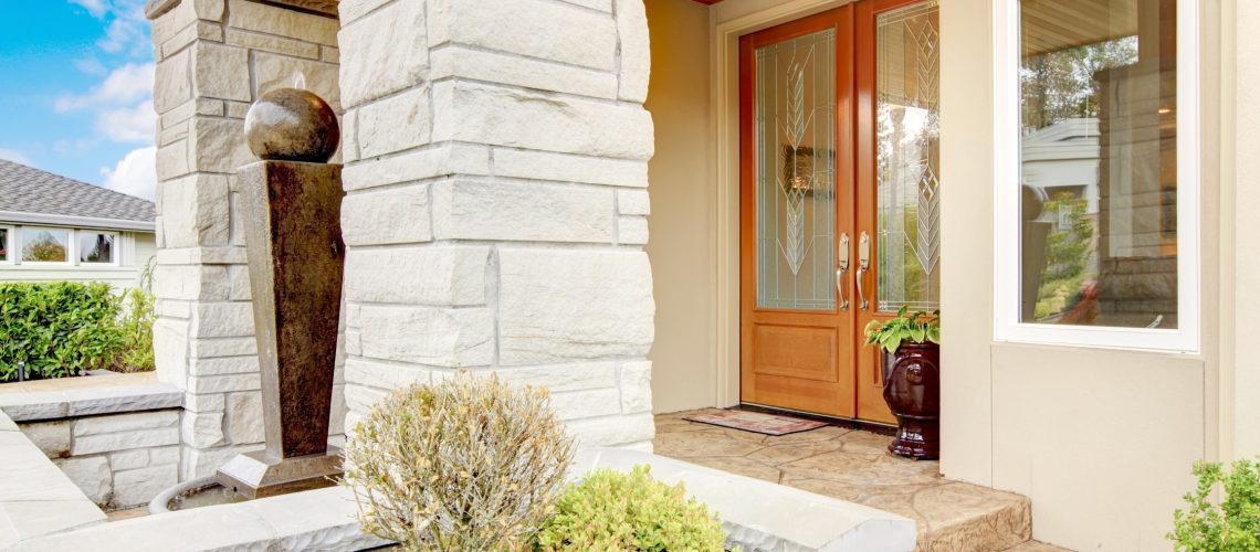 Luxury house entrance porch with stone column trim and stained wood door.